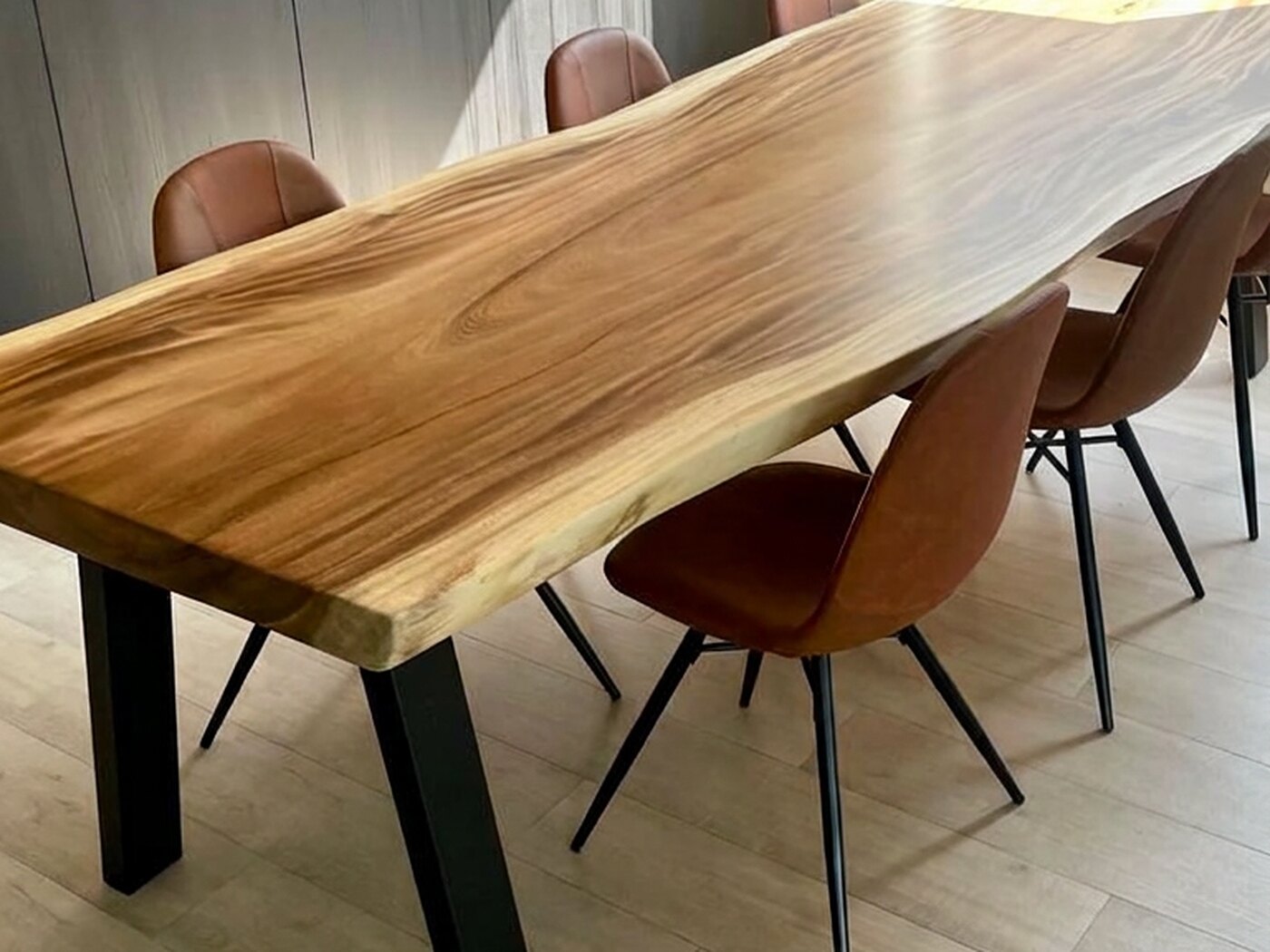 A live-edge Suar table with tan leather chairs down both sides, set against a wall of grey full-height joinery with a long picture shelf above